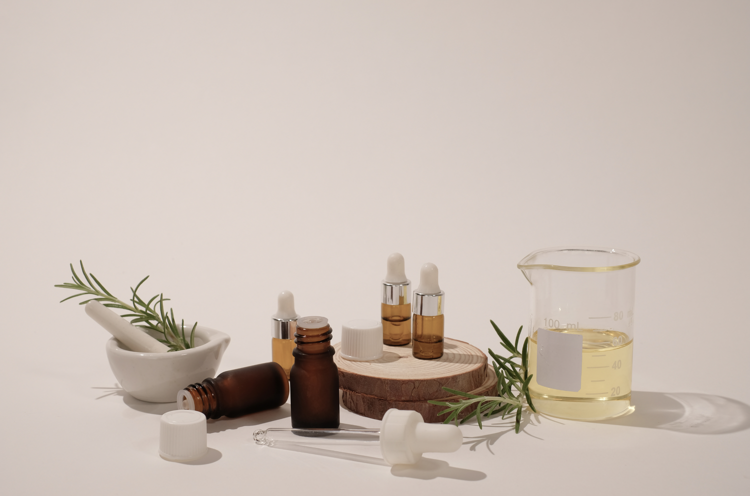 Glass product bottles on wood pedestal surrounded by green ingredients