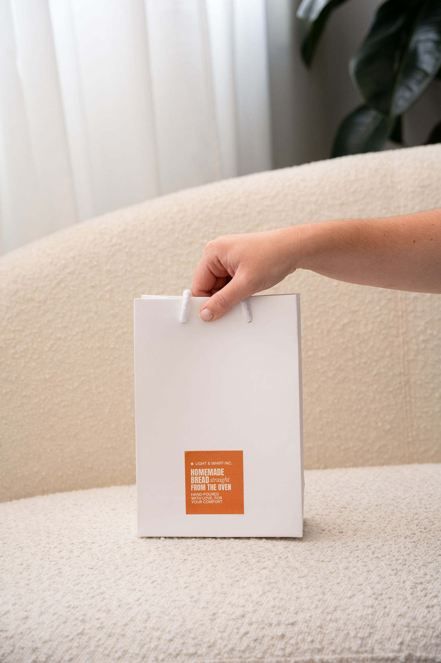 Model hand holding a branded bag on a neutral couch