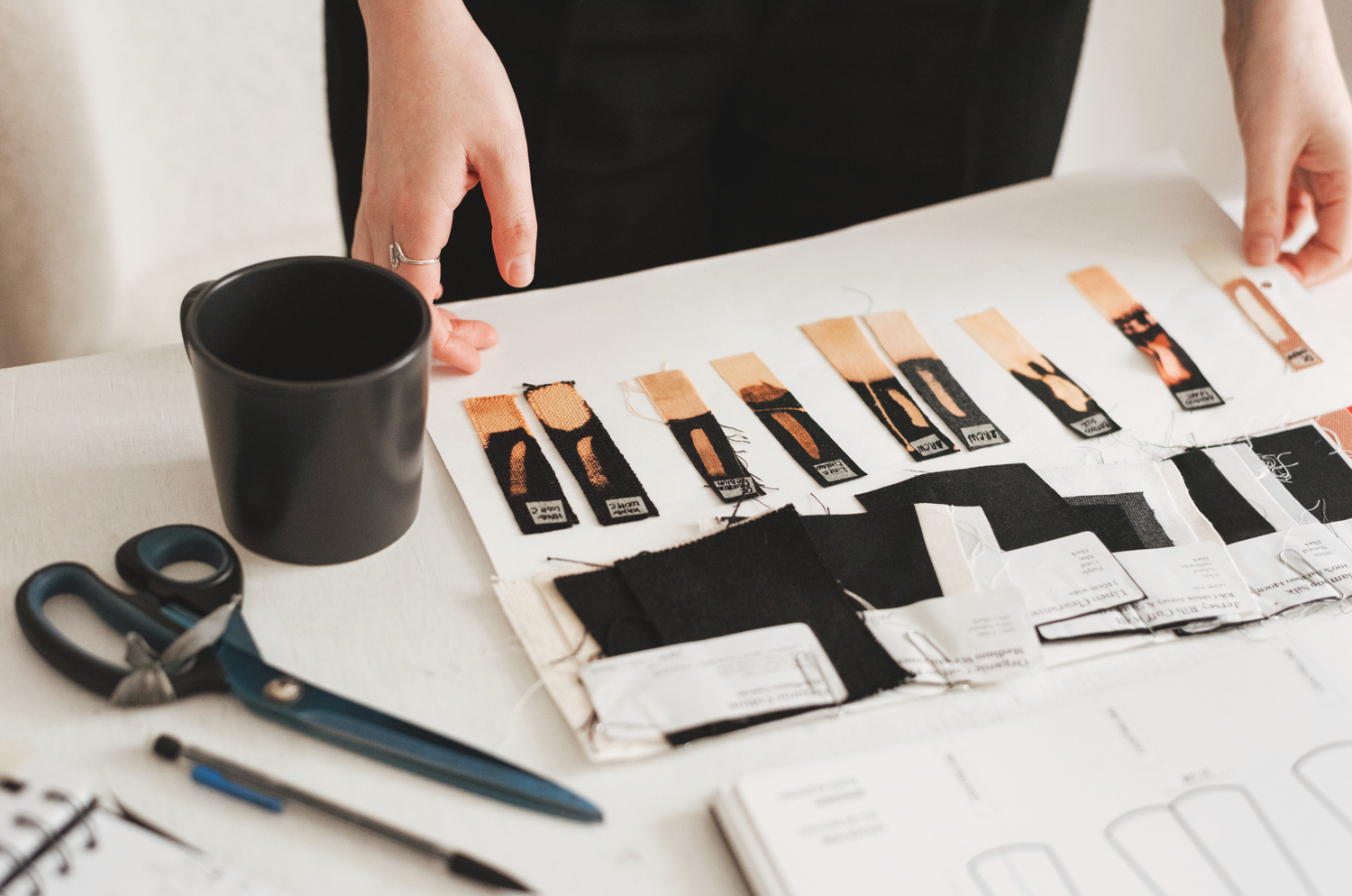 Model holding fabric samples with a coffee cup, scissors, pencil and journal on a desk