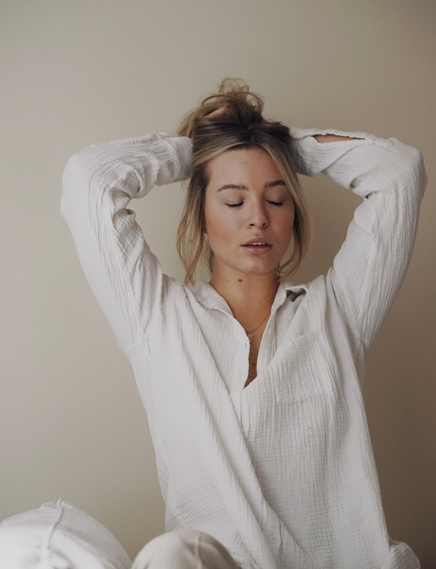 Model wearing all white holding hair up with hands