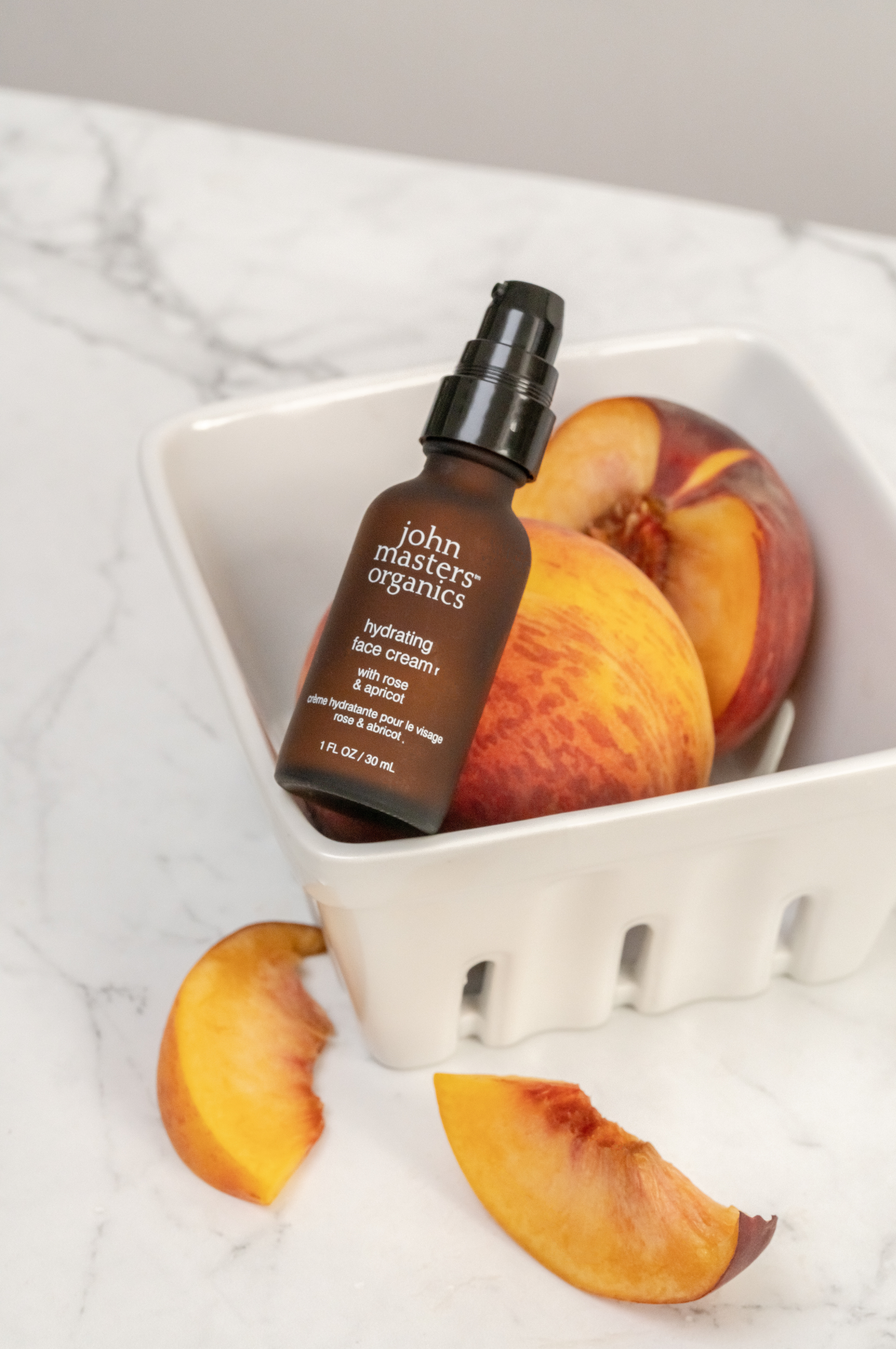 John Masters Organics Hydrating Face Cream in a glass fruit container with peaches