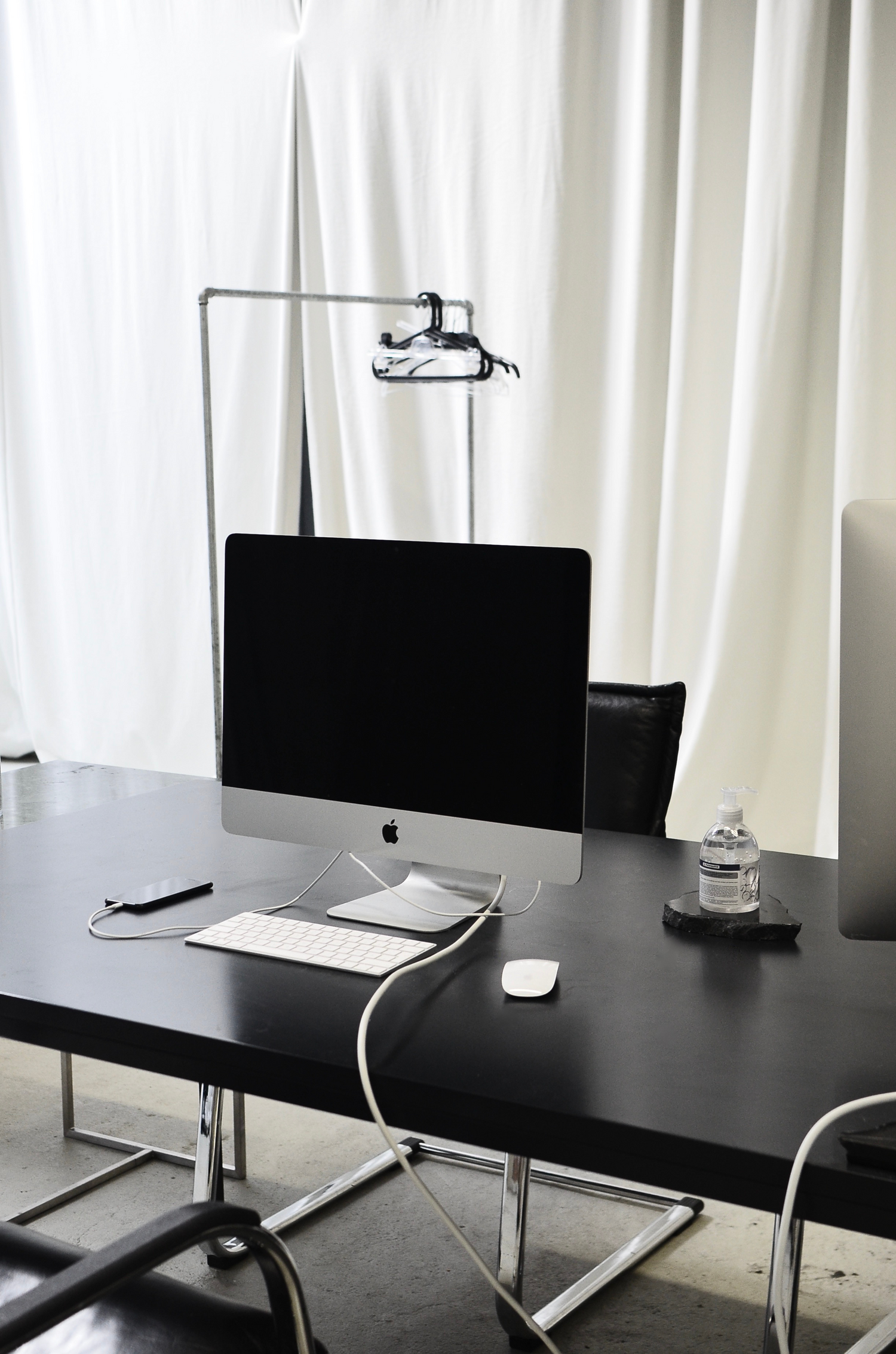 Black desk with an Apple monitor, iPhone, keyboard, mouse, and bottle of water on it