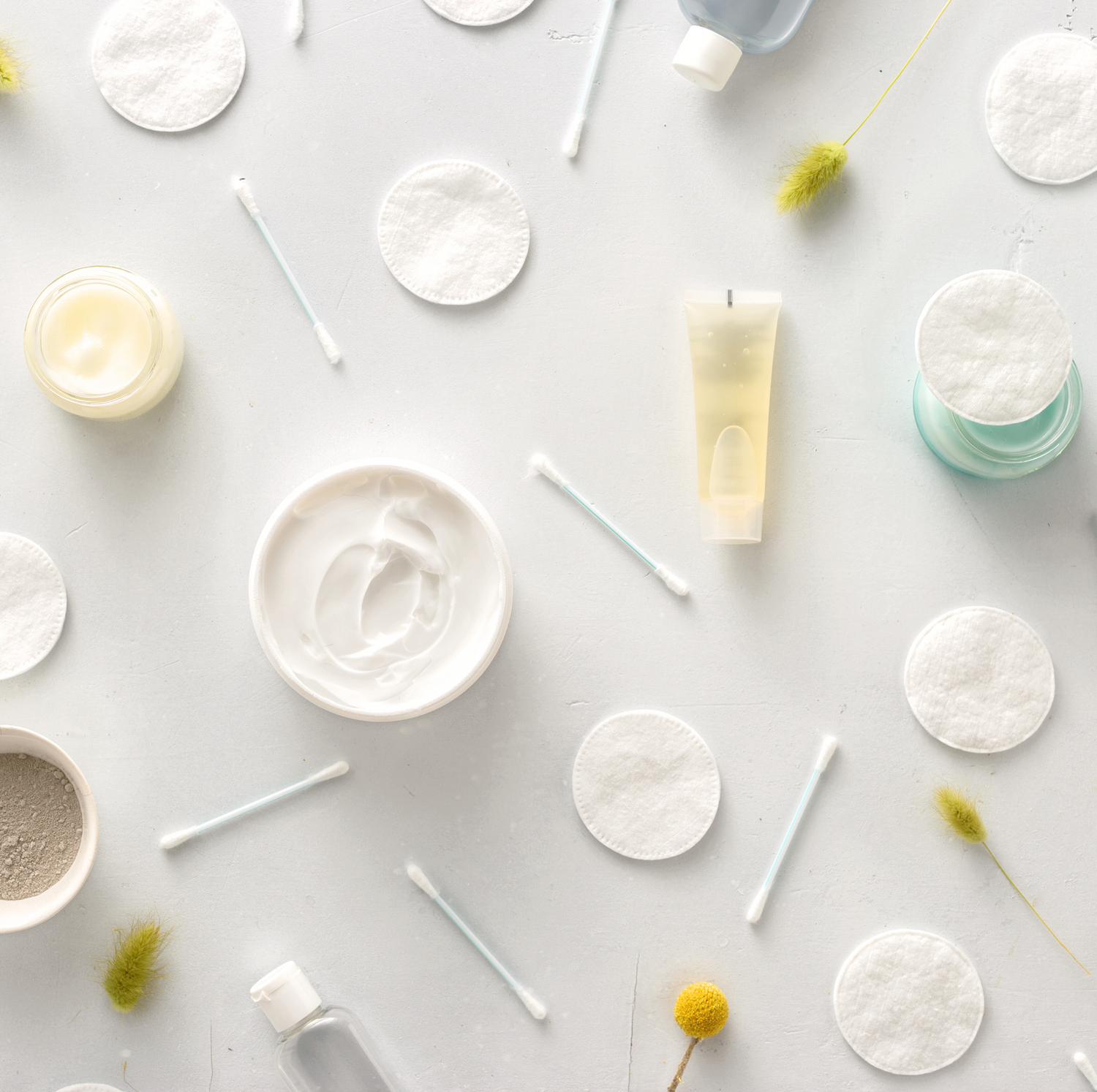 Cotton rounds, q-tips, product jars, product bottles, and ingredients laying on a neutral background