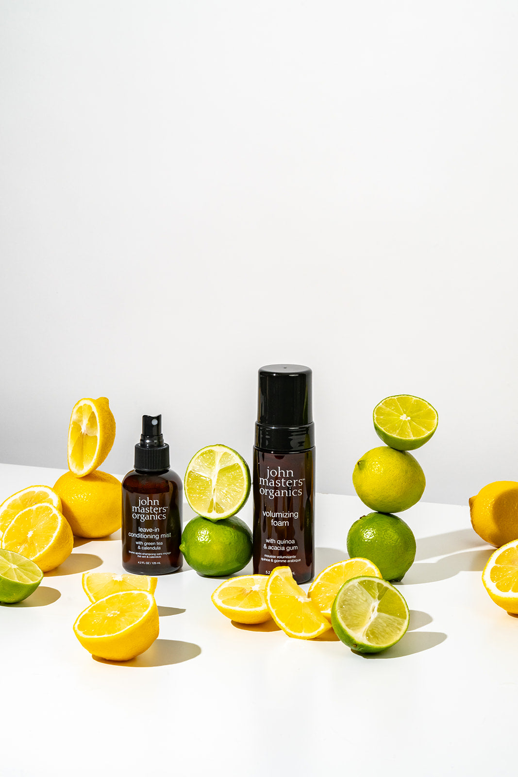 John Masters Organics Leave-In Conditioning Mist and Volumizing Foam surrounded by lemon and lime slices