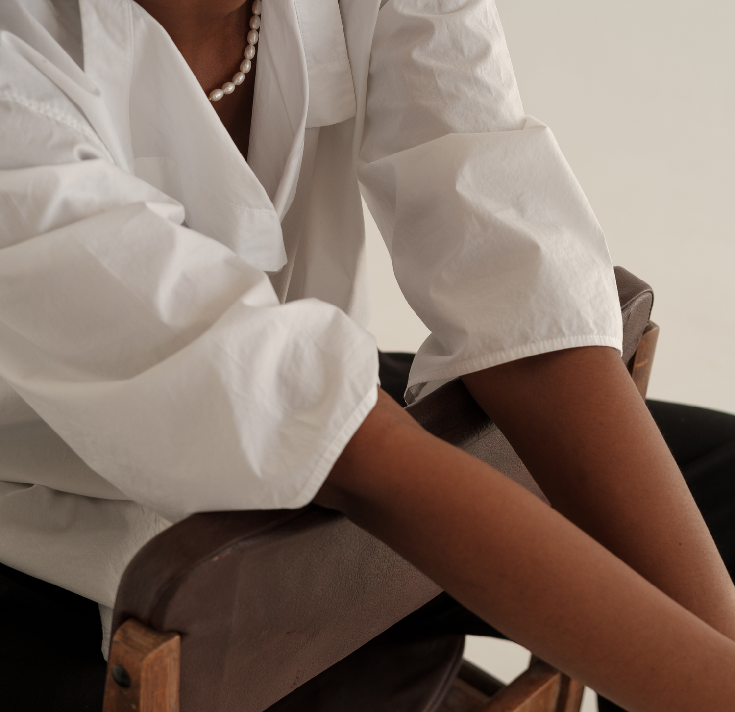 Model sitting on a chair backwards with arms over the top of the chair, wearing a white button down