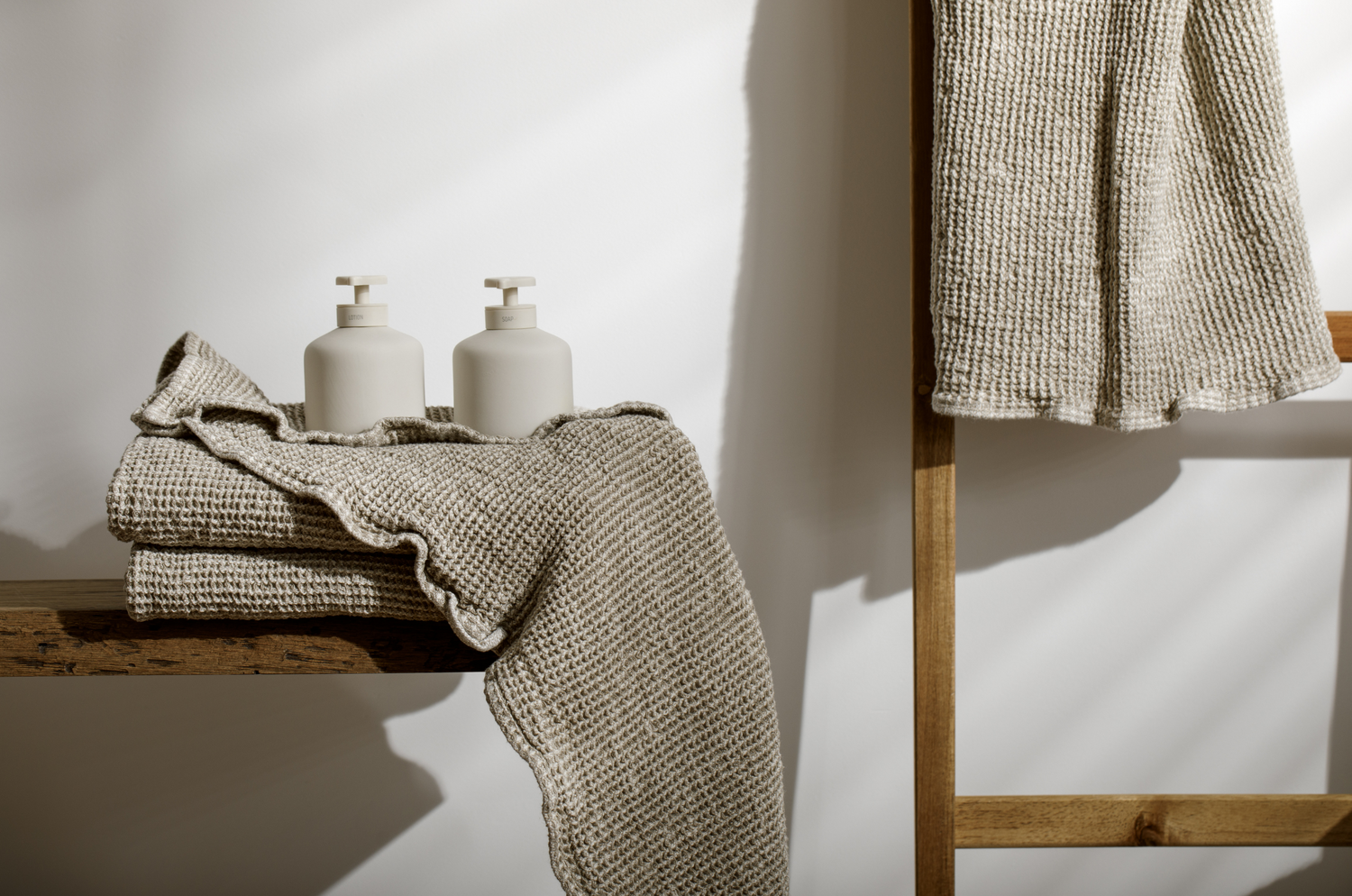 Towel stack with two soap dispensers sitting on them and a ladder with another towel hanging from a rung