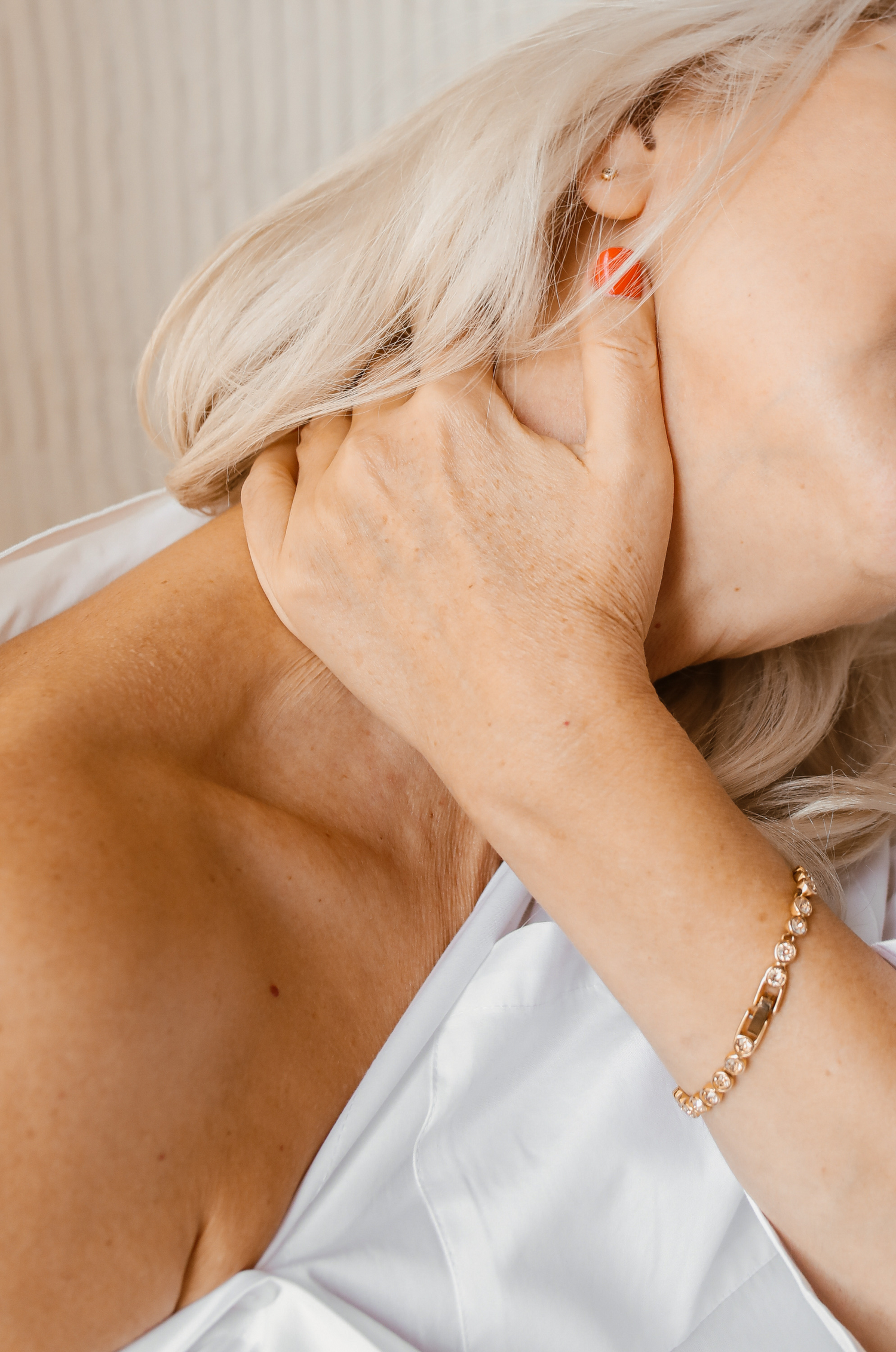 Model wearing white top and diamond bracelete, stretching neck with their hand on their neck