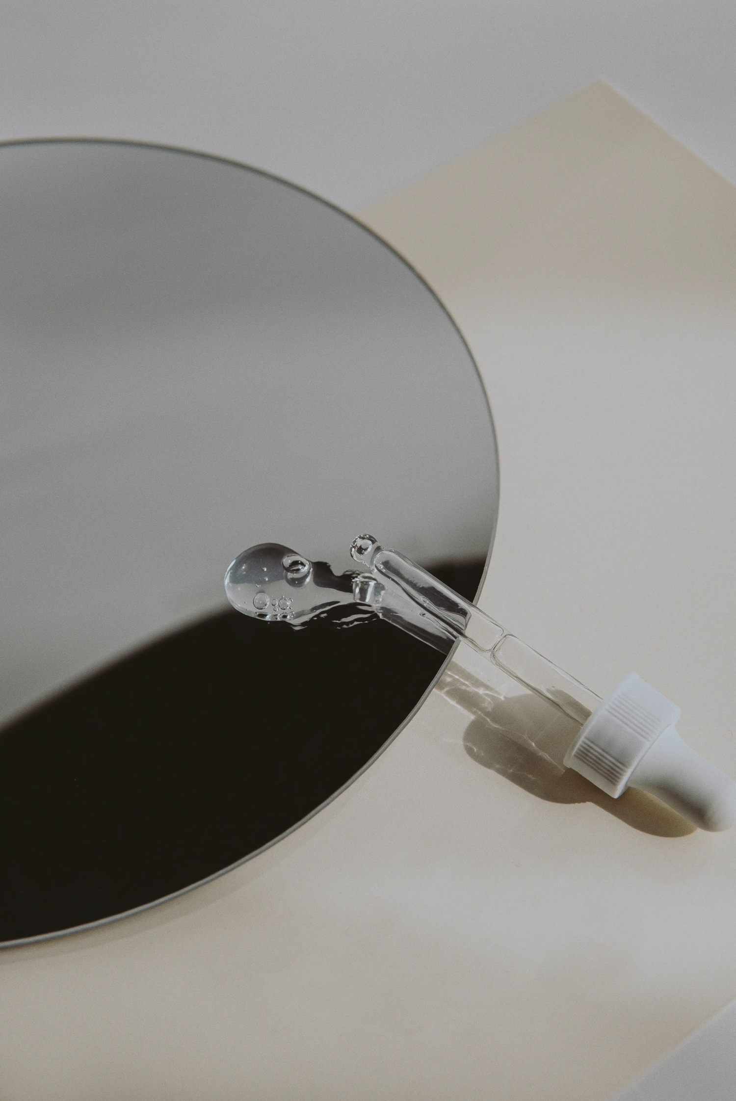 Serum dropper laying on a circular mirror with serum drop on the mirror