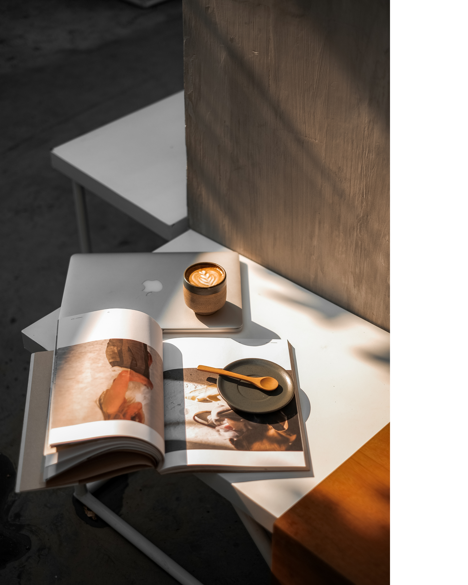 Open magazine with a plate and spoon resting on the page surrounded by a laptop and coffee on a white desk