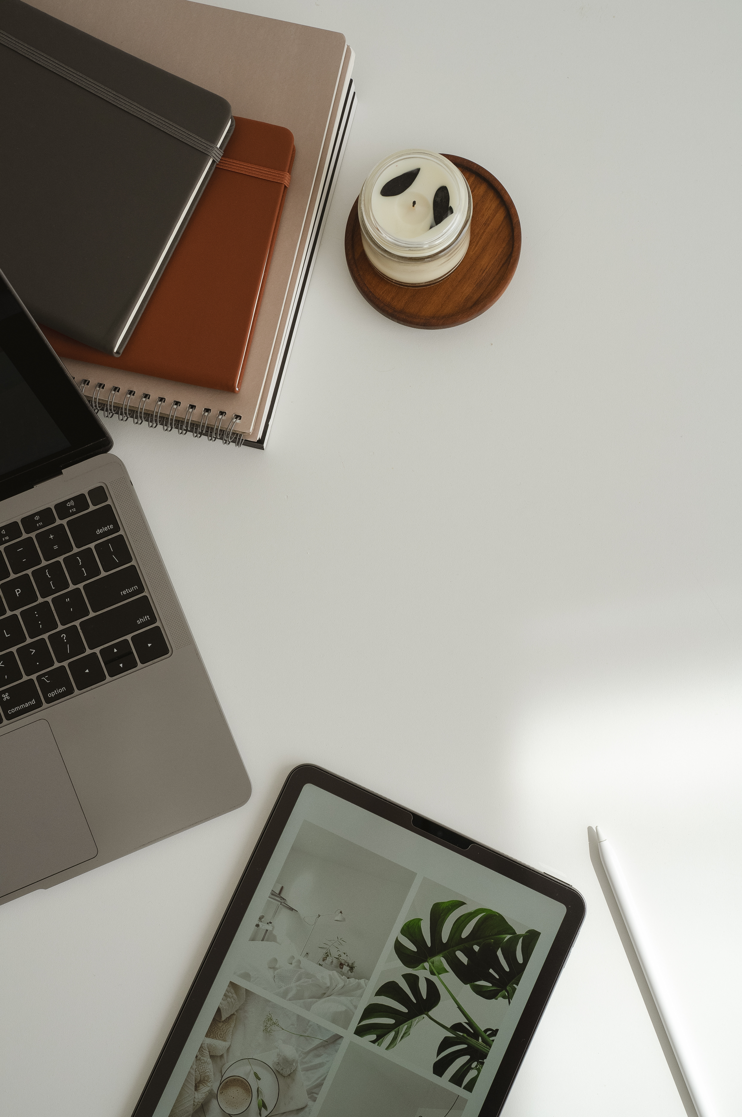 Laptop, iPad, Apple Pencil, notebooks, and a candle on a white table